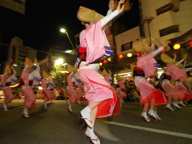 Awa Odori dancers in distinctive straw hats raise their arms in an illuminated line at Tokushima’s night festival