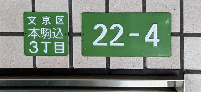 Two green residence-address plates on a wall in Honkomagome, Tokyo; the smaller names Bunkyo and Honkomagome 3, while the larger shows block 22 and residence number 4
