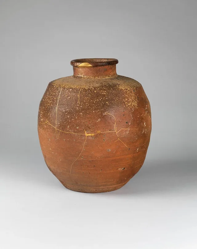 A brown seventeenth-century Shigaraki tea jar with fine branching lines of gold-lacquer repair across its body and neck