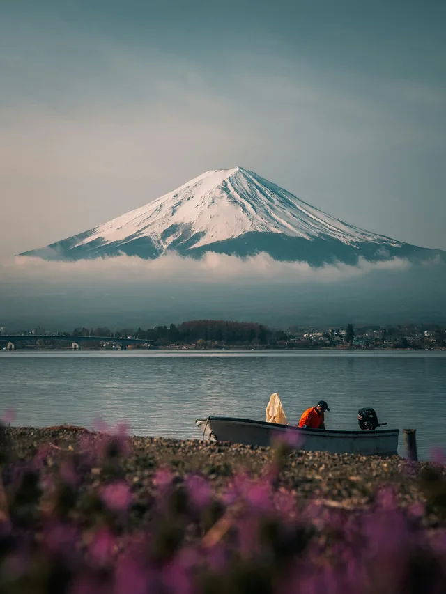 Snow-capped Mount Fuji above a calm lake and boat